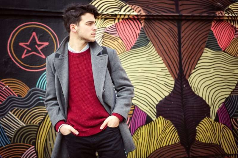 Young fashionable man standing in front of colorful wall. Autumn time outdoors.