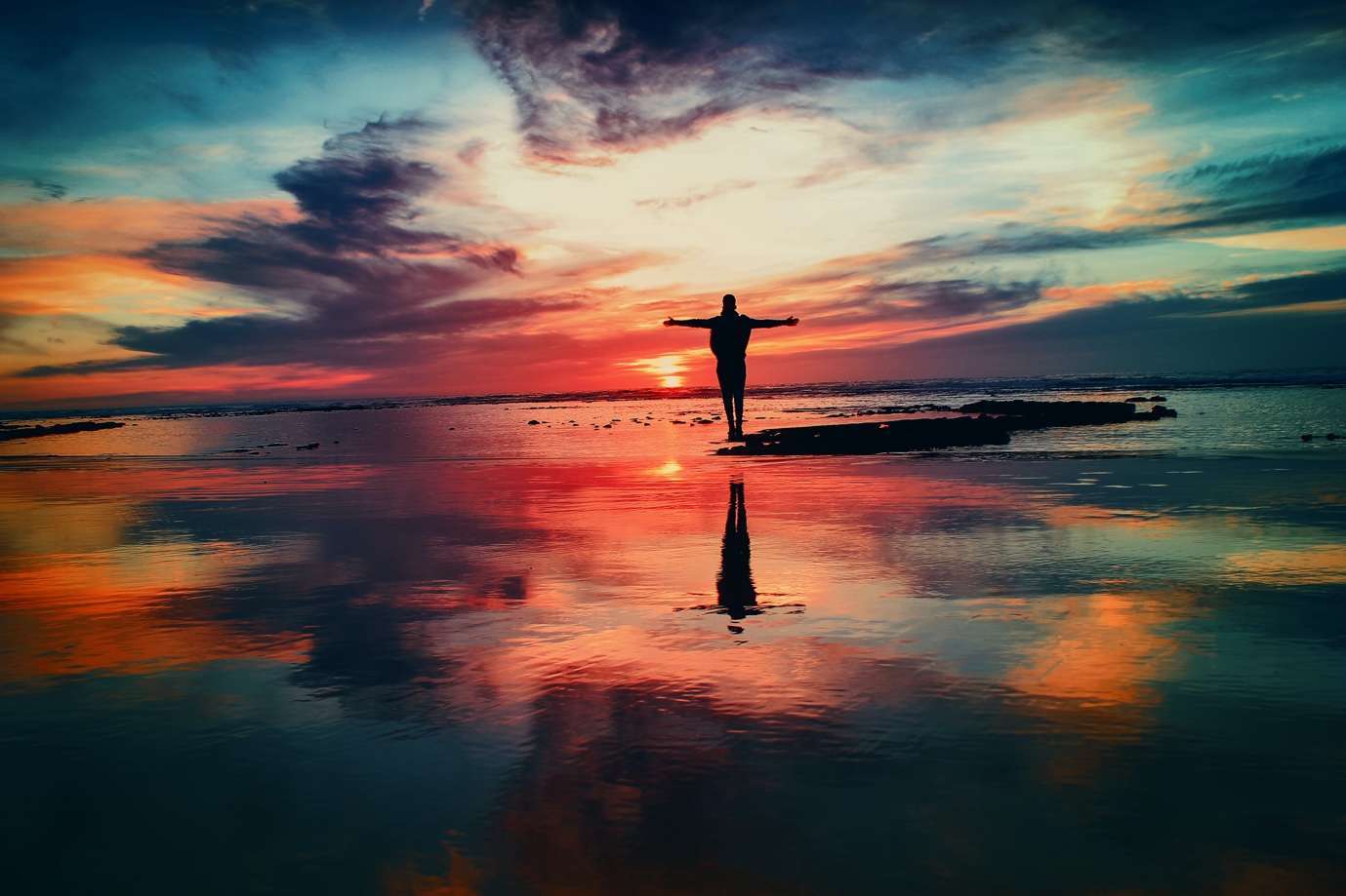 A person standing on a beach with their arms outstretched Description automatically generated